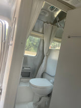 Interior of an RV rental: a bright, compact bathroom featuring a white toilet, shower, and windows for natural light.