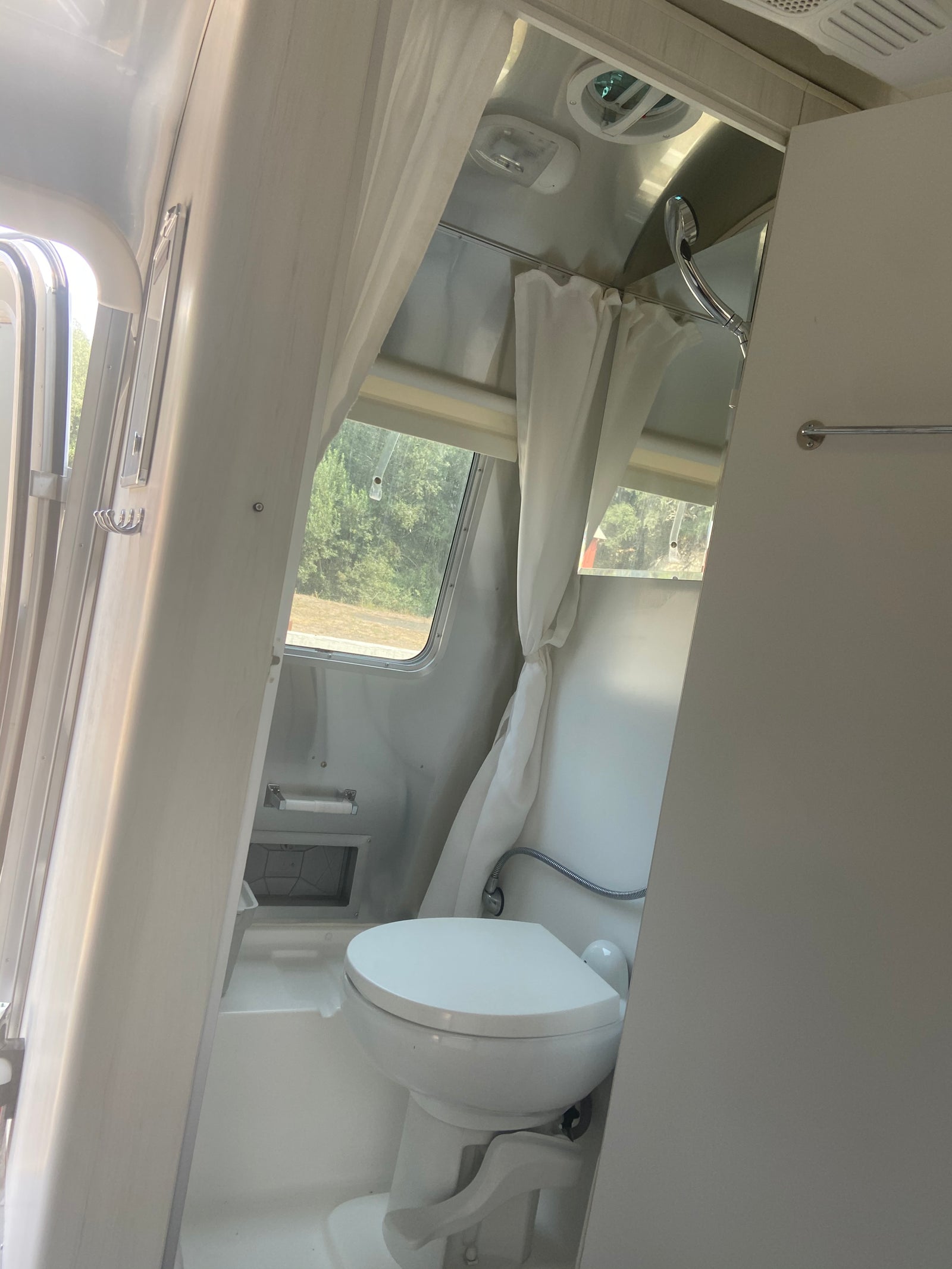 Interior of an RV rental: a bright, compact bathroom featuring a white toilet, shower, and windows for natural light.