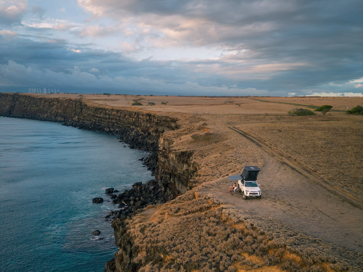  parked on a sandy track in Hawaii.|Overland RV rental SUV with rooftop tent set up at a stunning rocky beach campsite — photo 5