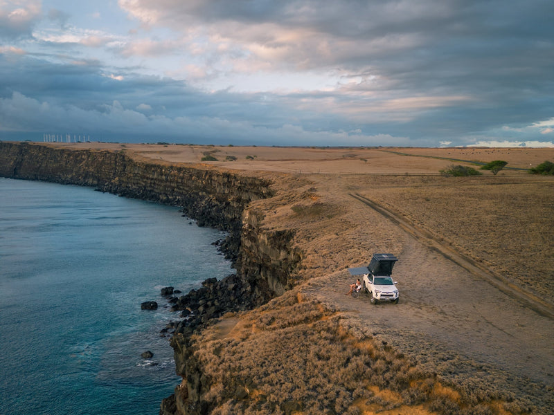  parked on a sandy track in Hawaii.|Overland RV rental SUV with rooftop tent set up at a stunning rocky beach campsite — photo 5