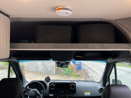 Looking forward in an rv rental: ceiling smoke detector, overhead storage, and vehicle dashboard. A safe and organized camper van cabin.