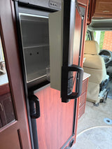 Inside an RV rental: empty refrigerator, top controls (DC/AC/GAS), and front cabin beyond. Compact travel features.