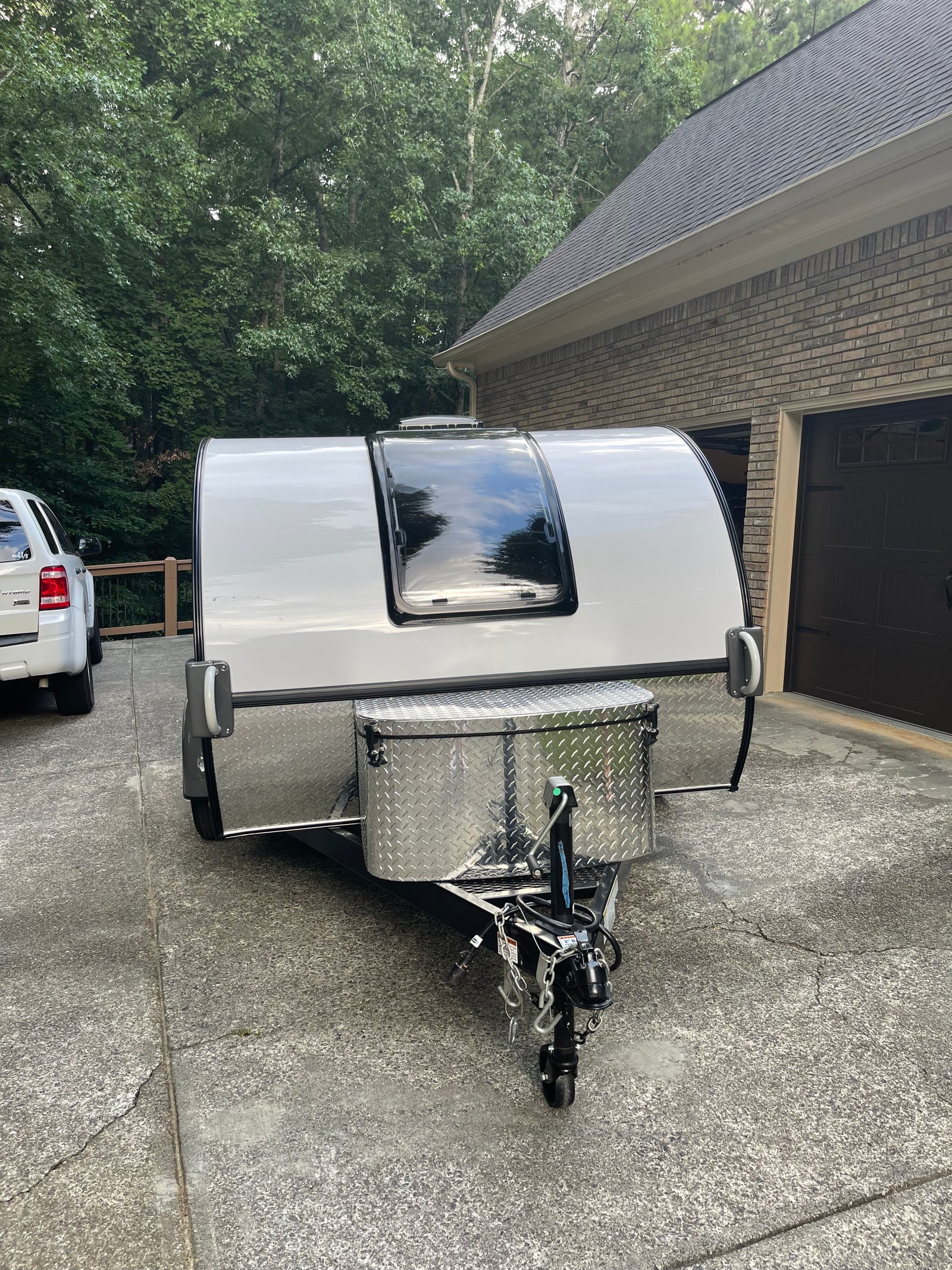 Compact white travel trailer, ideal for an rv rental adventure, parked in a driveway. Features a large front window & storage box.