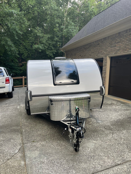 Compact white travel trailer, ideal for an rv rental adventure, parked in a driveway. Features a large front window & storage box.