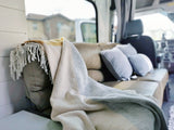 Experience comfort in this RV rental: a cozy interior featuring a comfy sofa, blue pillows, and striped blanket.