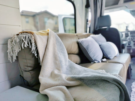 Experience comfort in this RV rental: a cozy interior featuring a comfy sofa, blue pillows, and striped blanket.
