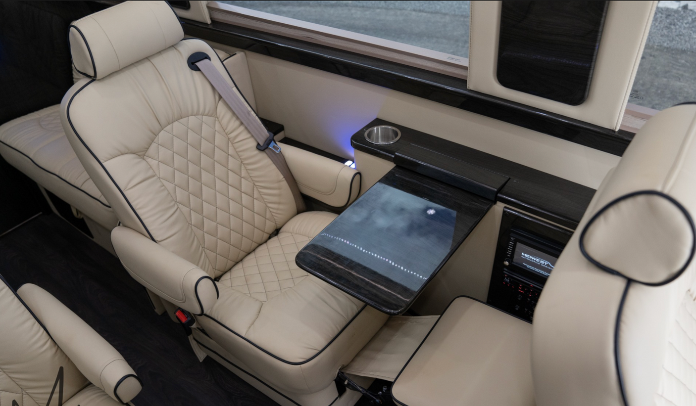 Plush cream leather interior of a luxury RV rental, featuring quilted captain's chairs, a pull-out table, and ambient lighting.