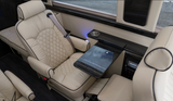 Plush cream leather interior of a luxury RV rental, featuring quilted captain's chairs, a pull-out table, and ambient lighting.