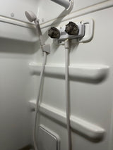 Interior of a compact white RV rental shower with handheld shower head, hot/cold faucet, and integrated shelving.