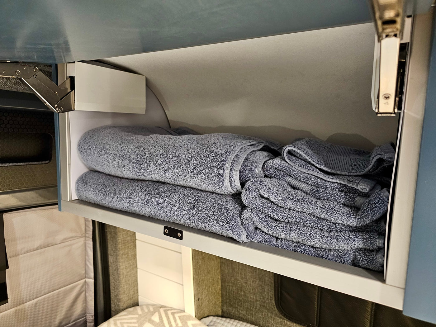 Soft blue towels organized in an overhead cabinet in an RV rental. Practical, space-saving storage for travel essentials. — photo 20
