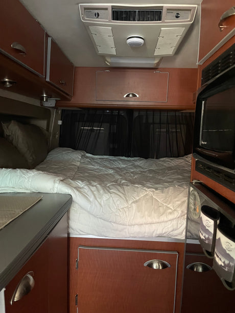 This rv rental offers a comfortable sleeping area with a bed, pillows, overhead cabinets, air conditioning, and microwave.