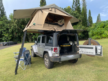 This Jeep RV rental, featuring a deployed rooftop tent, ladder, and camping chairs, is ideal for overland adventures.