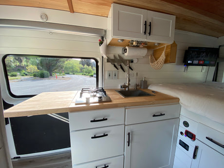 RV rental: Modern camper van kitchen with stove, sink, and storage, showcasing a compact living space.
