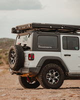 White Jeep overlanding vehicle with rooftop tent on desert terrain, ready for your RV rental adventure.