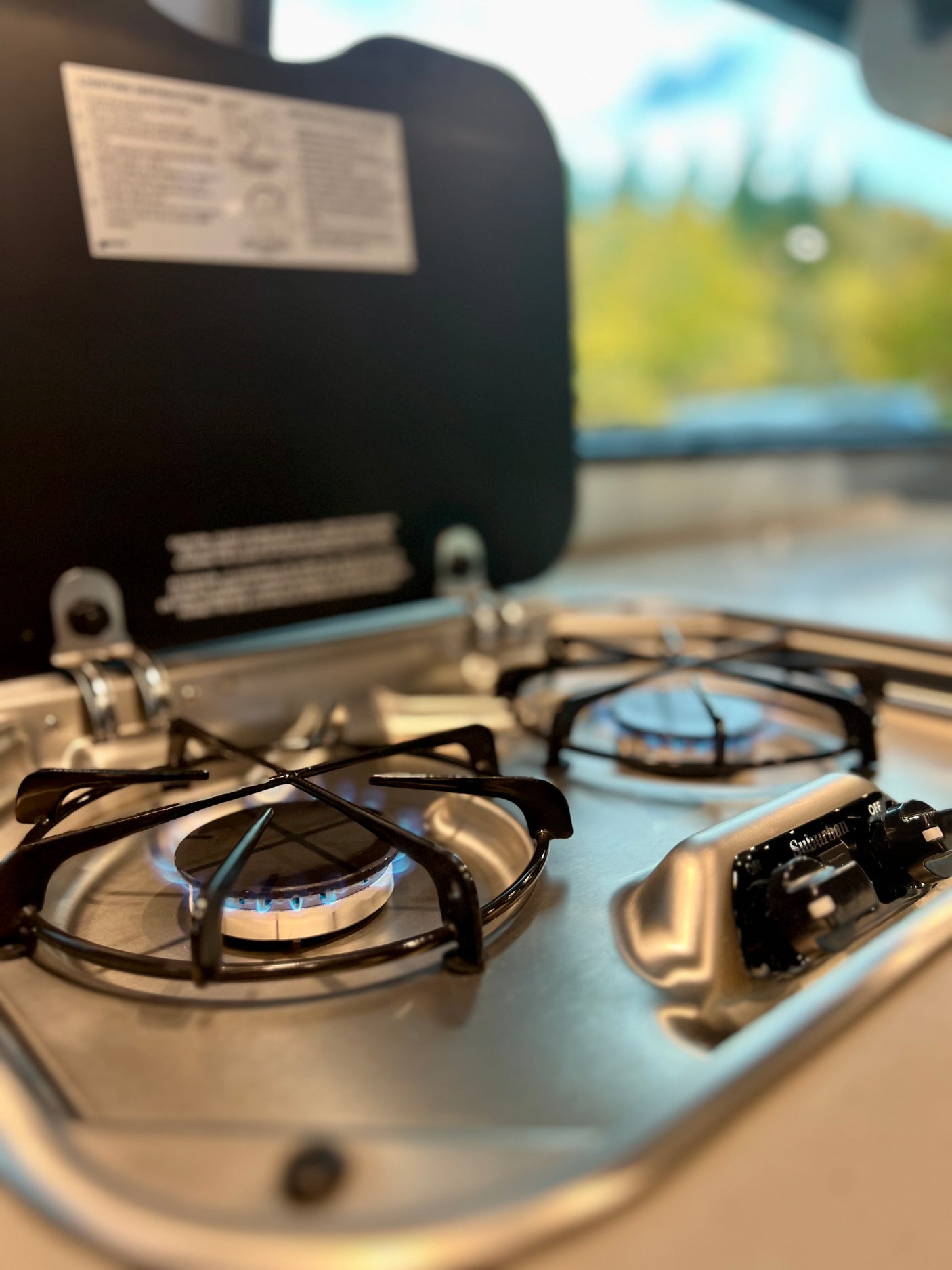 This RV rental kitchen features a clean, two-burner gas stove, one burner lit with a blue flame, perfect for campsite cooking.