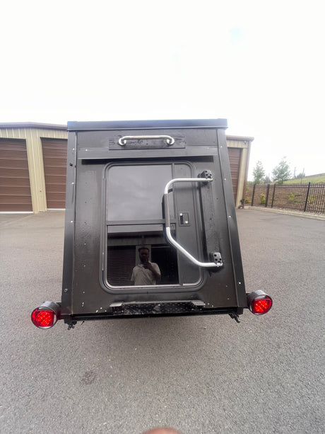 Rear view: compact black RV rental trailer, door, window, grab handles, and red taillights. Ready for adventure.