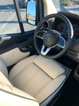 Luxury RV rental: detailed view of the driver's cabin with cream leather seats, a Mercedes-Benz steering wheel, and dashboard.