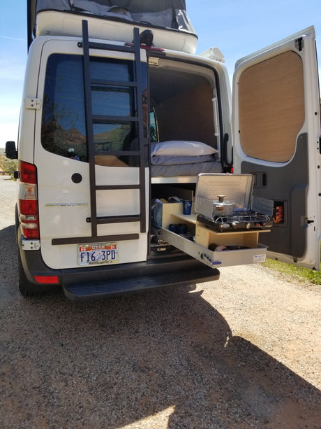Rear view of a converted Sprinter van, an RV rental with a pull-out outdoor kitchen and bed for camping.