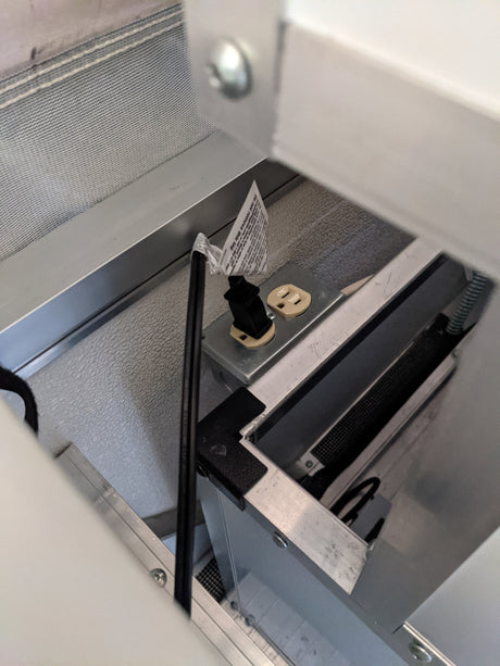 Essential for your RV rental: An electrical outlet with a power cord, a "Do not remove" tag, within an aluminum-framed compartment.