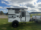 Sunray Sport RV rental: a white and gray teardrop camper trailer hitched to a truck, ready for adventure by a scenic lake and hills.