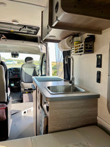 RV rental interior: compact kitchen with sink, paper towels, cleaning supplies, driver's cab, and seating.