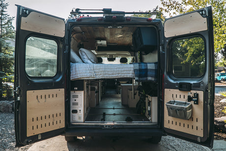 Rear view of a customized camper van interior, perfect for RV rental adventures. Features a cozy bed and smart storage.
