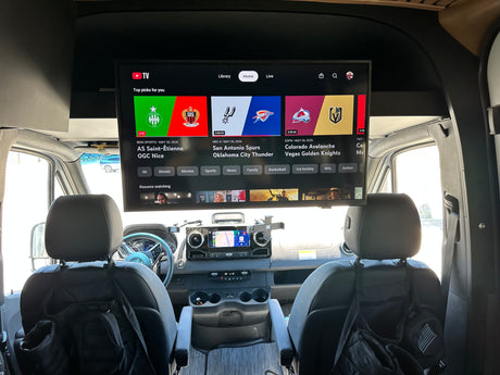 RV rental interior: A large TV above the dash displays YouTube TV with live sports. Front seats and vehicle controls visible.