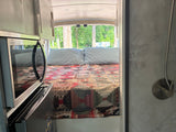 Explore this rv rental interior: a cozy bed with quilt, microwave, and a shower corner, set for relaxing road trips.