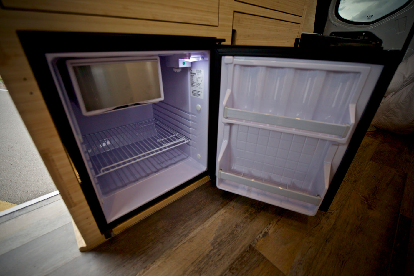 Open, empty mini-fridge inside an RV rental, featuring a compact freezer and shelves. Perfect for road trips.