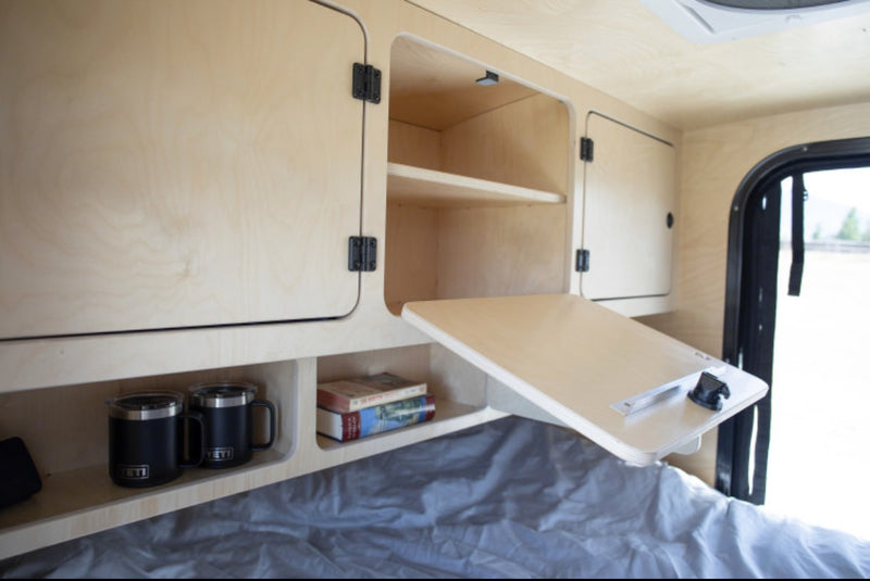 Cozy RV rental interior: wooden cabinets, a fold-down table, and cubby storage with mugs and books. — photo 15