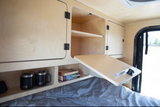 Cozy RV rental interior: wooden cabinets, a fold-down table, and cubby storage with mugs and books.