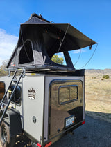 Compact RV rental: A grey Escapade Camper with a black NatureNest rooftop tent deployed in a scenic Colorado landscape.