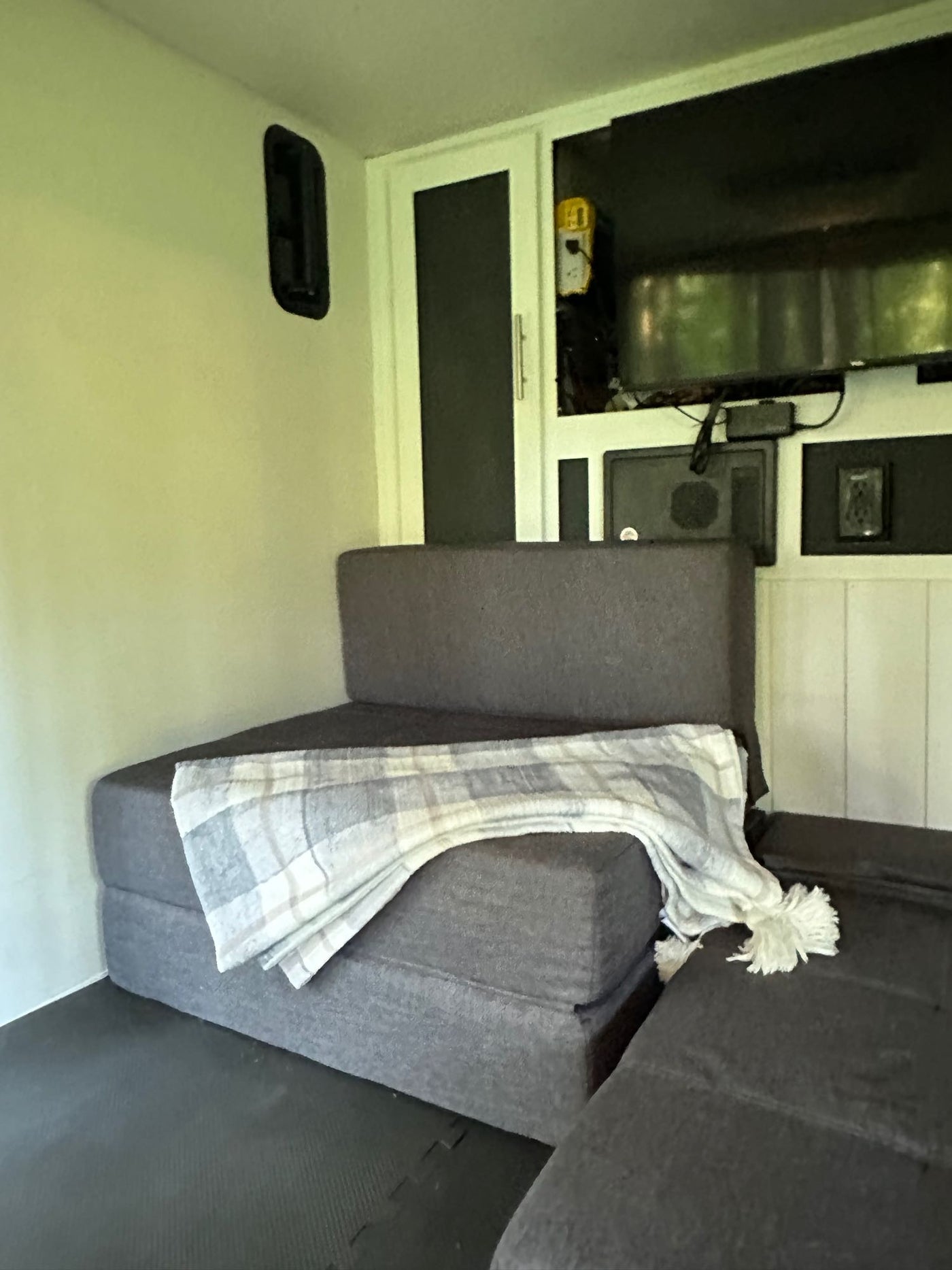 Inside an rv rental: dark grey modular seating with a plaid blanket, a mounted TV, and black floor mats create a functional space. — photo 10