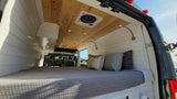 Cozy RV rental van conversion interior with comfy bed, wood ceiling, recessed lighting, and reading lamps.