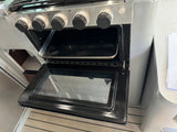 An open stainless steel oven with a baking tray and control knobs, part of an RV rental kitchen setup.
