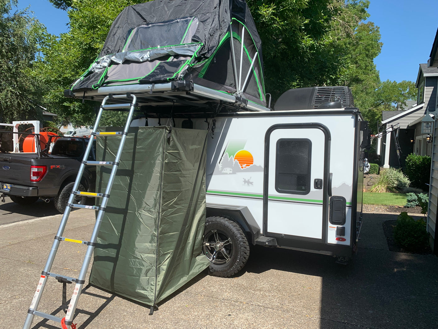 RV rental: White camper trailer features a rooftop tent, ladder, and privacy annex. Pickup truck parked next to it.