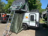 RV rental: White camper trailer features a rooftop tent, ladder, and privacy annex. Pickup truck parked next to it.