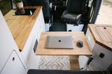 Inside an RV rental, a sleek mobile workspace with a laptop on a pull-out table, adjacent to a compact kitchen.