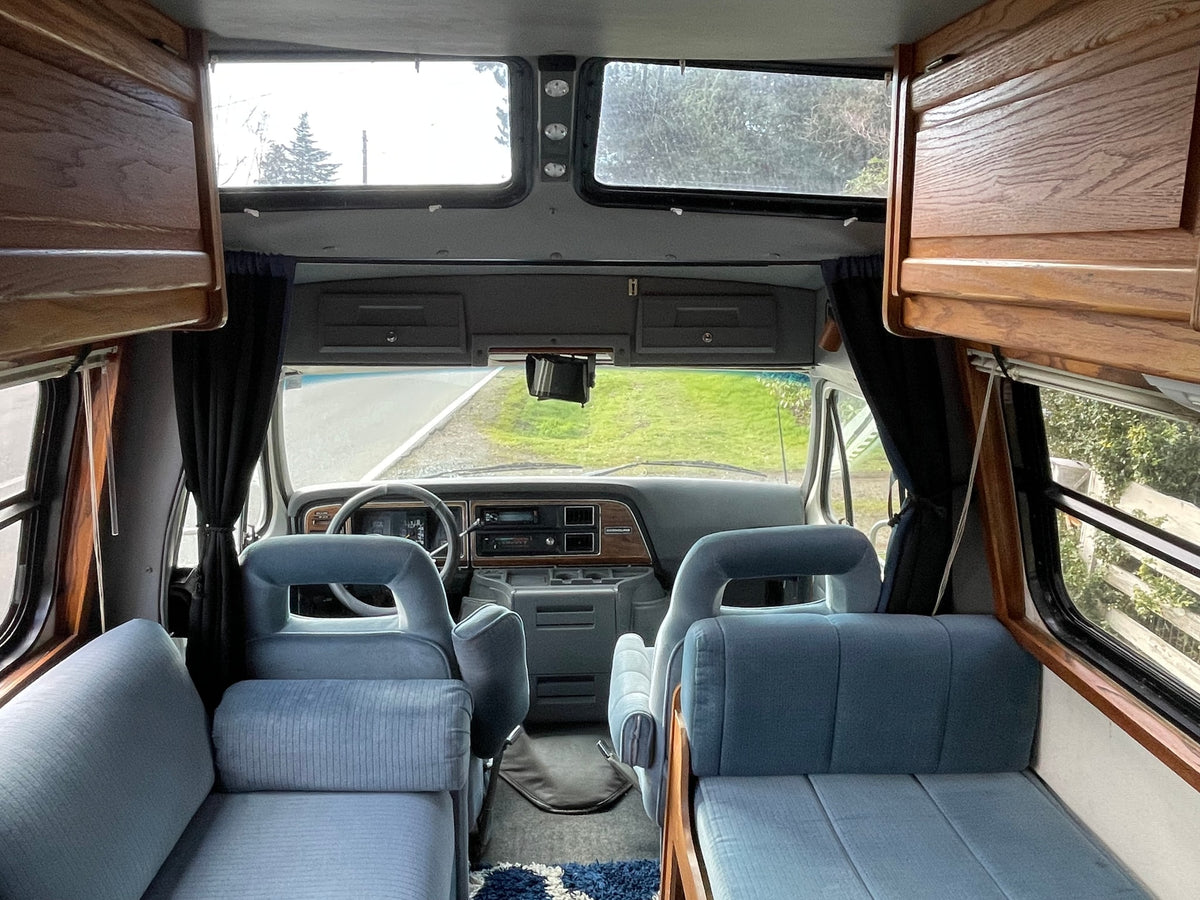 Inside an rv rental: view from the back, showing blue upholstered seats, wooden cabinets, and the cockpit with road view. — photo 13