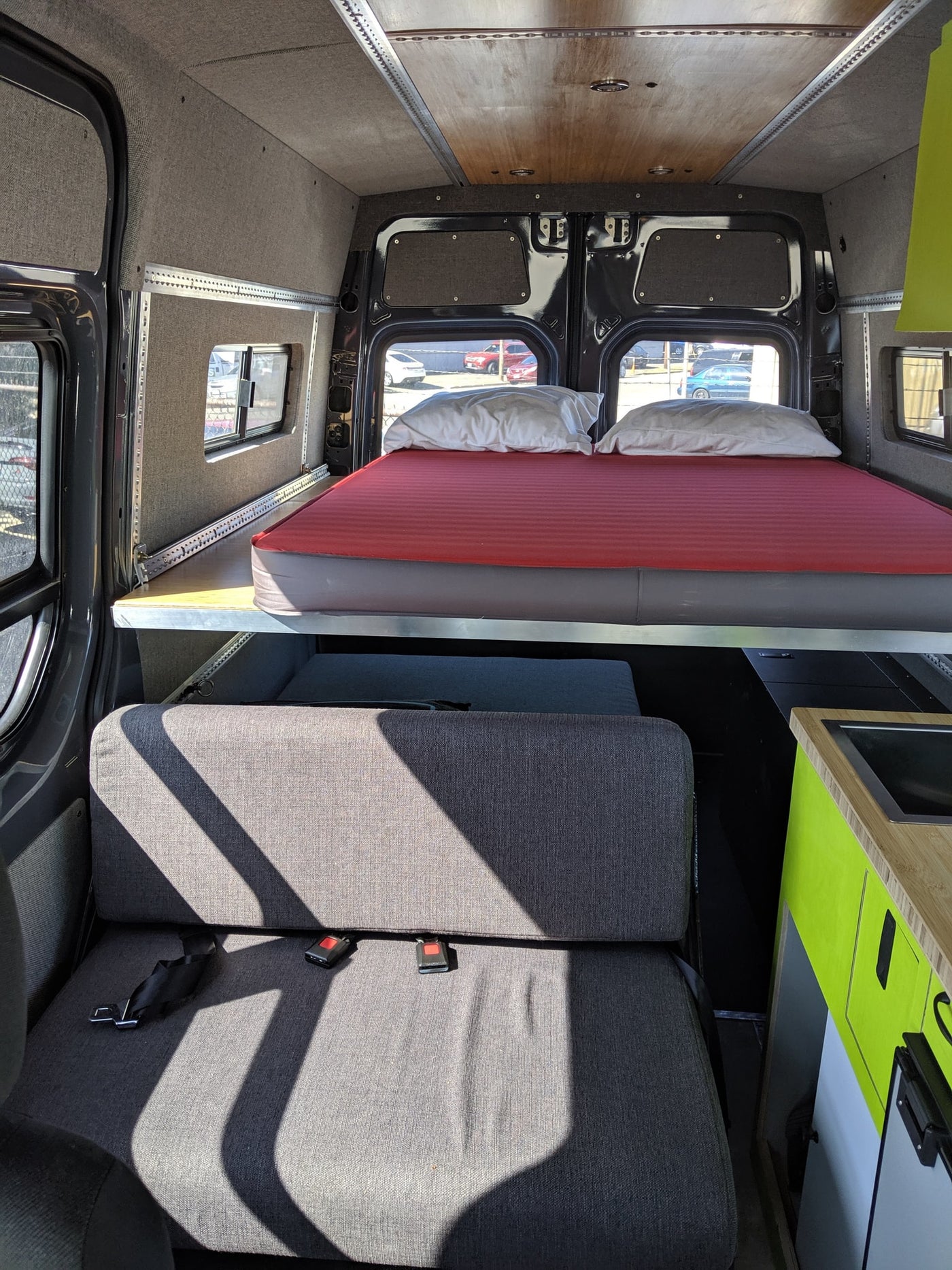 RV rental: Bright camper van interior with a raised bed, comfortable upholstered seating, and a lime green kitchenette. — photo 7