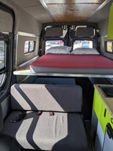 RV rental: Bright camper van interior with a raised bed, comfortable upholstered seating, and a lime green kitchenette.