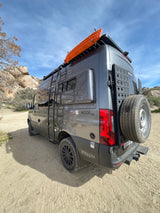 A gray 4x4 Sprinter adventure van (rv rental) with roof rack, ladder, and spare tire, ready for off-road exploration.