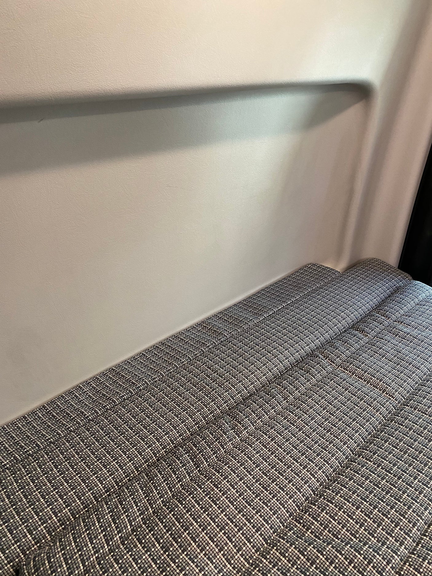 Inside an RV rental, a sleeping area with patterned gray cushions against a light, textured wall.