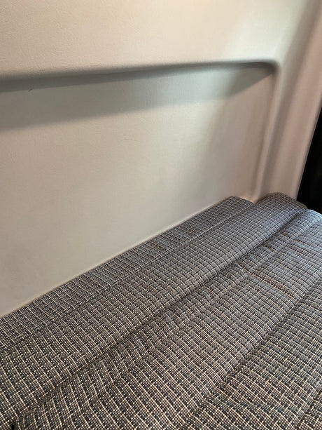 Inside an RV rental, a sleeping area with patterned gray cushions against a light, textured wall.