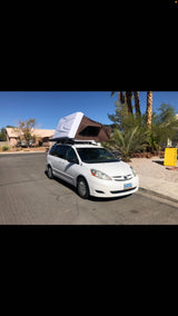 Explore with this compact RV rental: a white Toyota Sienna minivan featuring a deployed rooftop tent for camping.