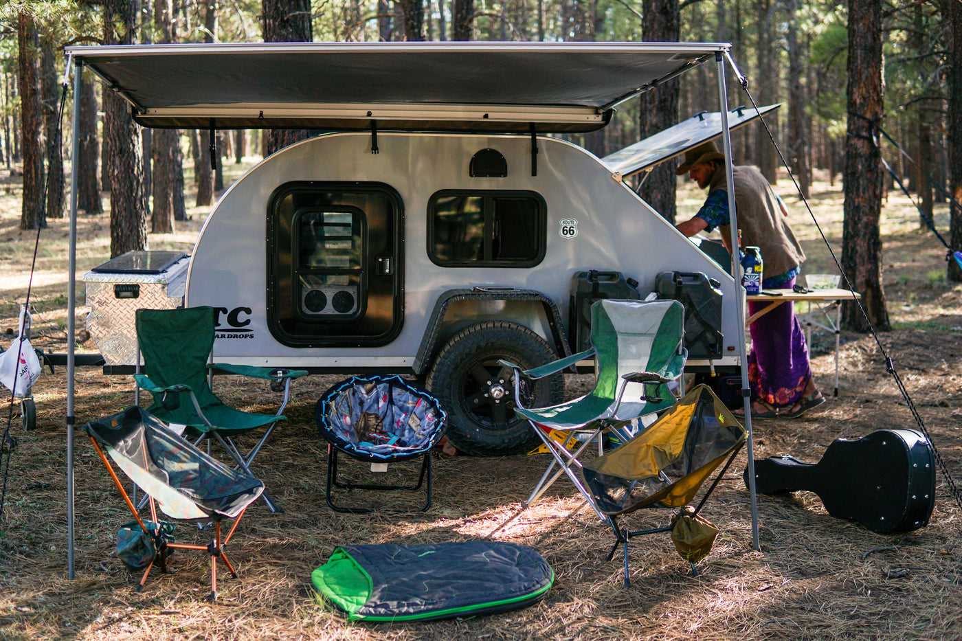 RV rental: a compact teardrop trailer set up at a shaded campsite, complete with chairs and a cooking area. — photo 14