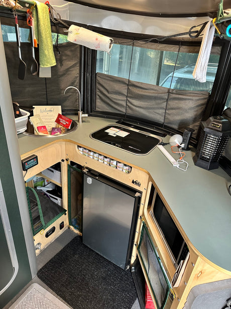 Inside a clean RV rental kitchen: sink, stove, fridge, utensils, and a welcome gift basket for your adventure.