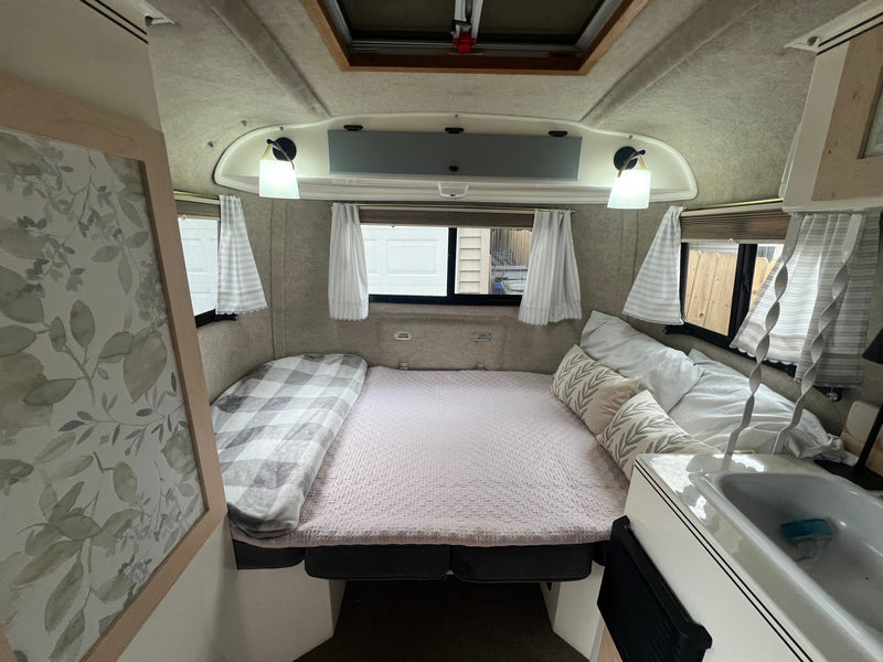 Explore this comfy RV rental bedroom area. Features a bed, leaf-patterned pillows, windows, and a compact sink. — photo 9