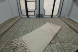 Experience an RV rental! This camper van's cozy bed, covered with a waffle-knit blanket, offers views from the rear doors.