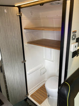 RV rental wet bath interior: compact design with a toilet, slatted wooden shelves, and a bamboo floor mat.